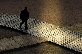 Silhouette of a man walking on a wooden pier at night