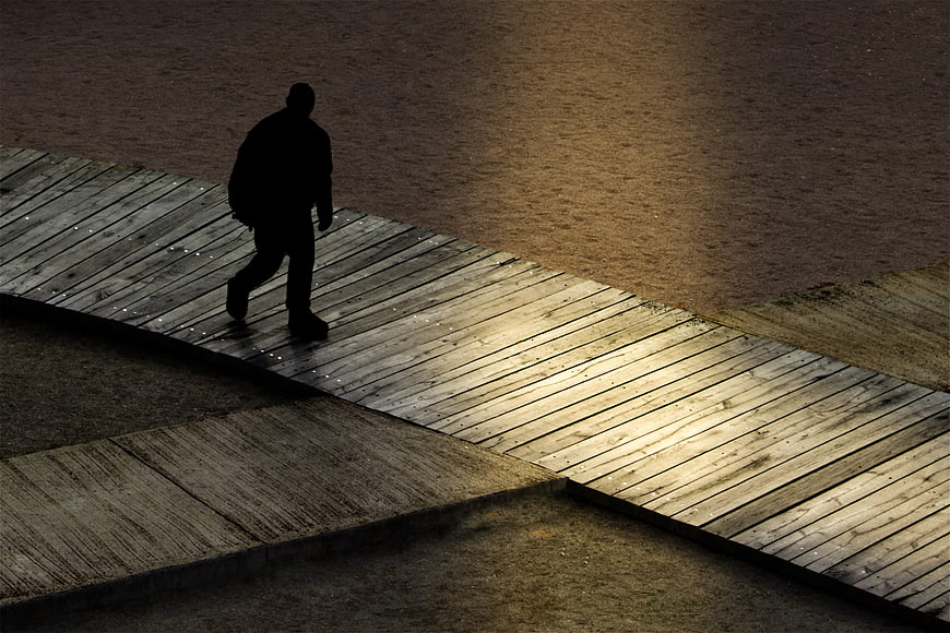 Silhouette of a man walking on a wooden pier at night