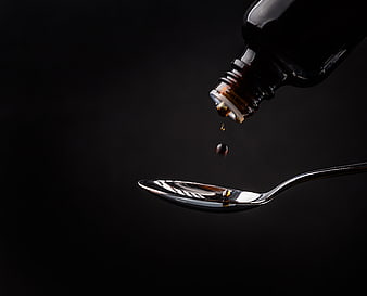 Dark amber liquid medicine dripping from bottle into spoon