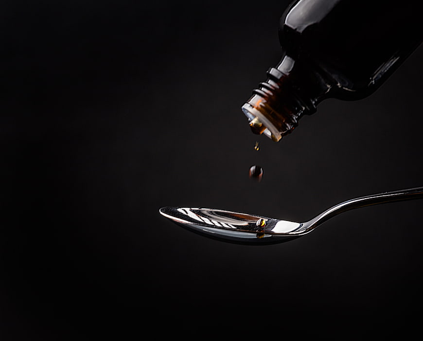 Dark amber liquid medicine dripping from bottle into spoon