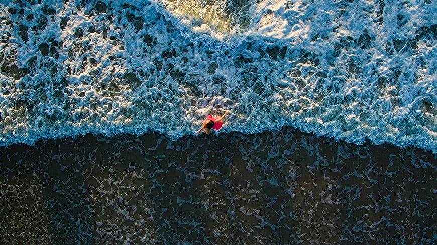 Aerial view of woman in red dress standing in ocean waves
