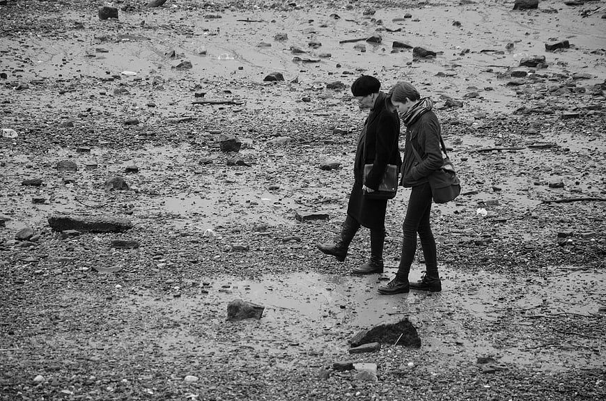 Two women walking on rocky riverbank in black and white