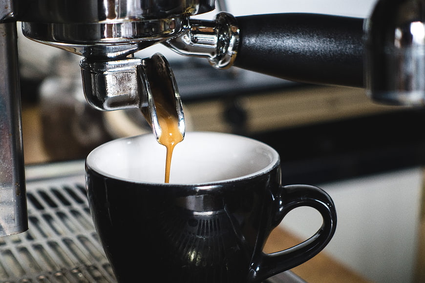 Espresso pouring from portafilter into black cup