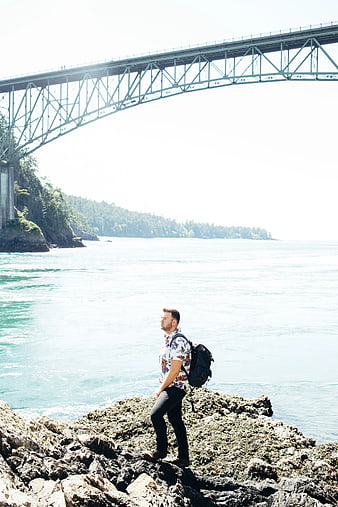 Man with Backpack Standing on Rocks Under Bridge
