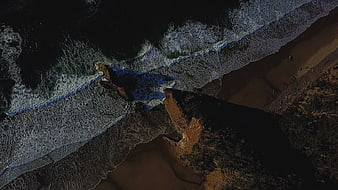 Aerial view of dark ocean waves crashing on a sandy beach at night