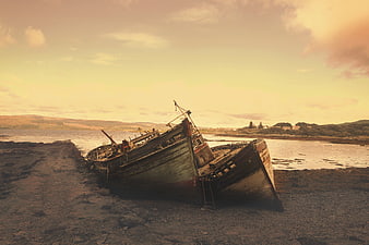 Abandoned wooden fishing boats on a rocky shore at sunset
