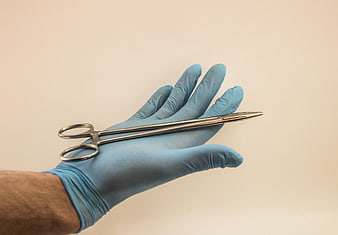 Blue Gloved Hand Holding Surgical Scissors Against Beige Background