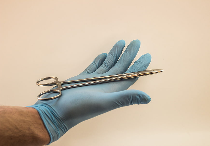 Blue Gloved Hand Holding Surgical Scissors Against Beige Background