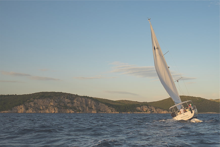 Sailboat Heeling on Blue Sea with Rocky Coastline