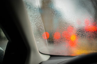 Raindrops on car window with blurred red traffic lights