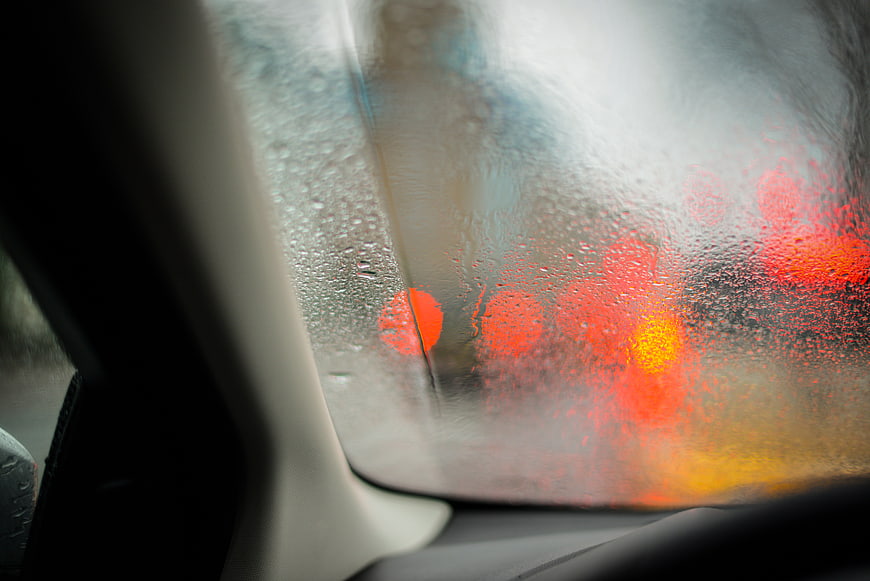 Raindrops on car window with blurred red traffic lights