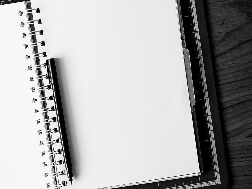 Black and white spiral notebook with pen on wooden desk