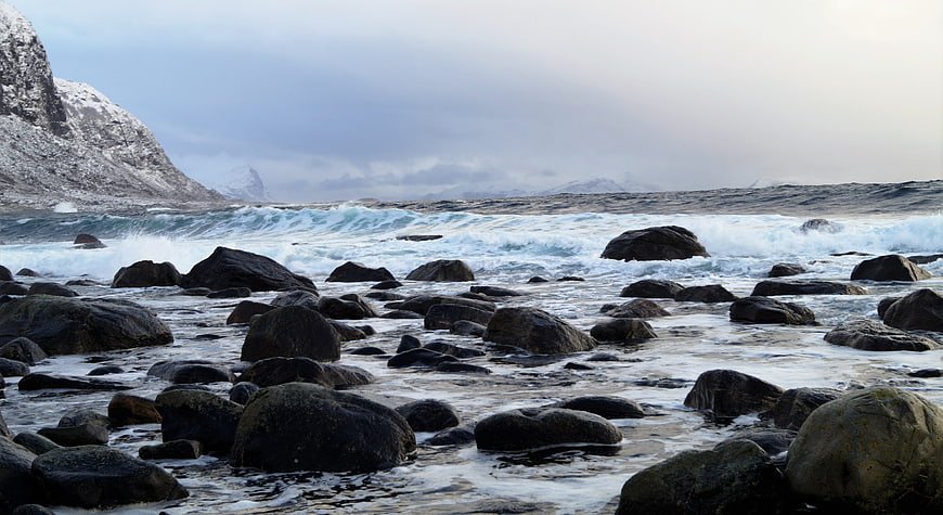 Dramatic Winter Coastal Landscape with Crashing Waves and Snowy Mountains