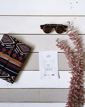 Flat lay of sunglasses, patterned wallet, and motivational quote on white wood