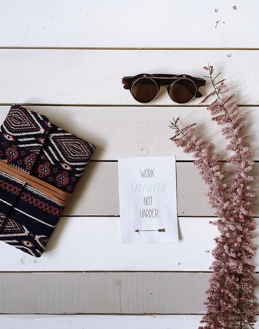 Flat lay of sunglasses, patterned wallet, and motivational quote on white wood