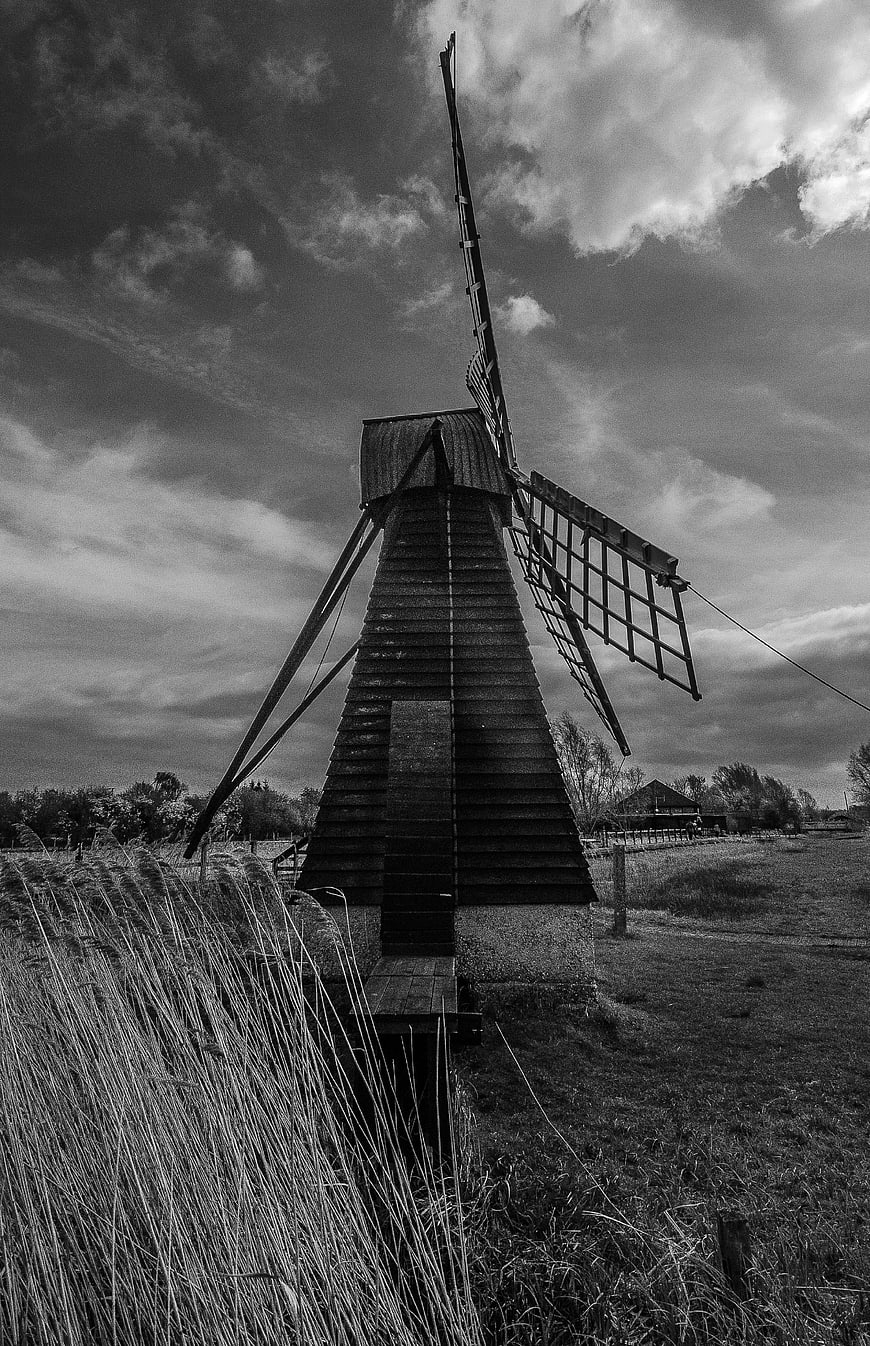 Black and white photo of old wooden windmill in rural landscape