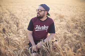 Man with beard and sunglasses sitting in golden wheat field