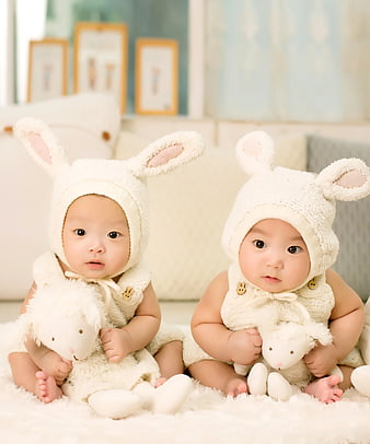 Adorable twin babies in white bunny costumes holding plush toys