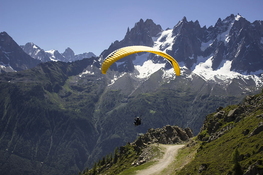 Yellow Paraglider Soaring Over Snowy Mountain Peaks