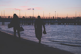 Silhouette of couple walking on beach at dusk with pier