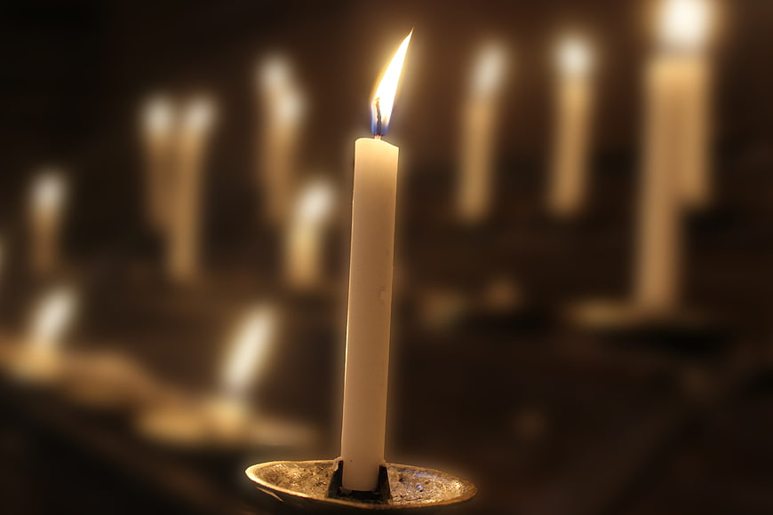 Single lit white candle with blurred background bokeh