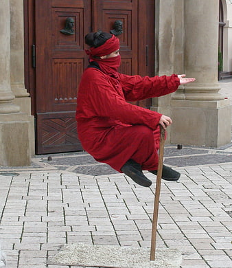 Street performer balancing on a stick in red costume