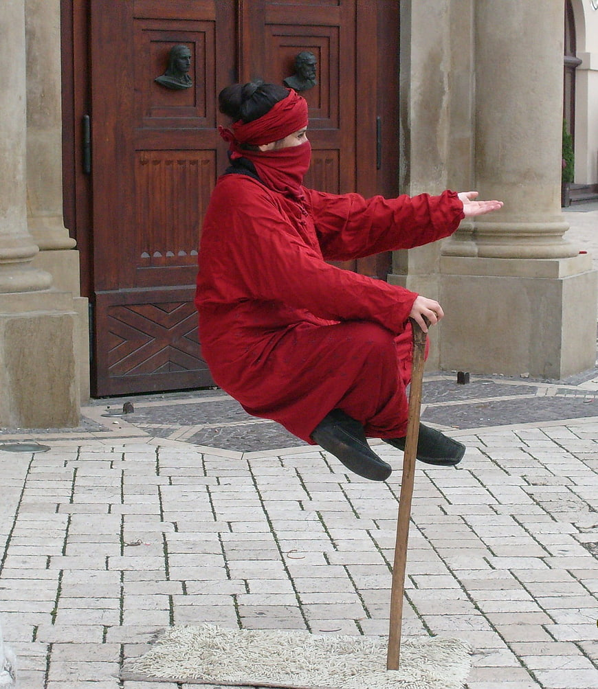 Street performer balancing on a stick in red costume