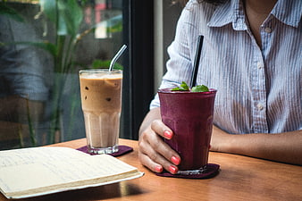Woman holding purple smoothie and iced coffee at cafe