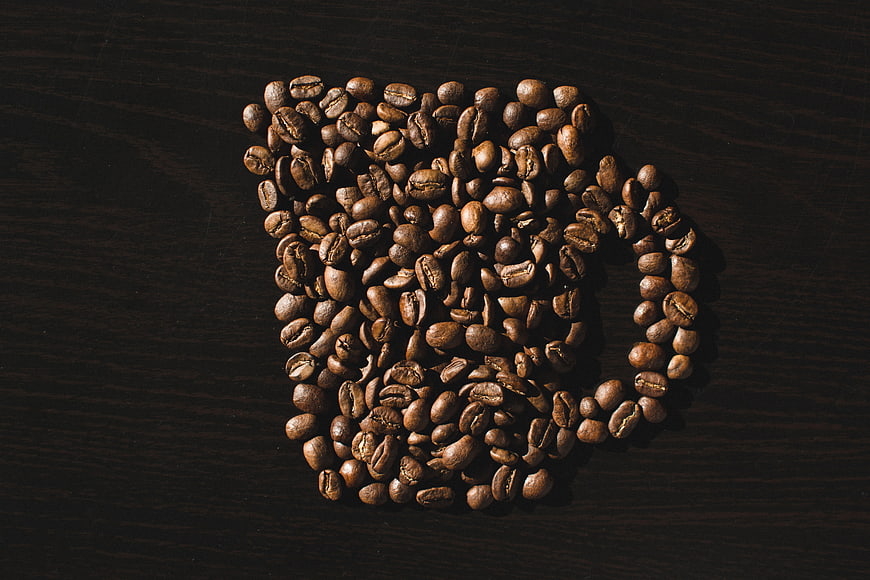 Coffee beans arranged in a mug shape on dark wood