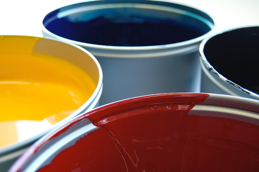 Close-up of open paint cans with vibrant red, yellow, blue, and black paint