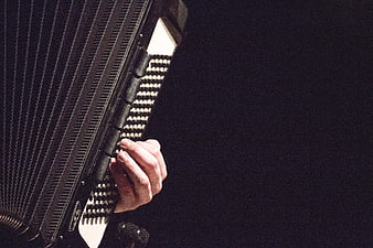 Close-up of hand playing accordion keys on dark background