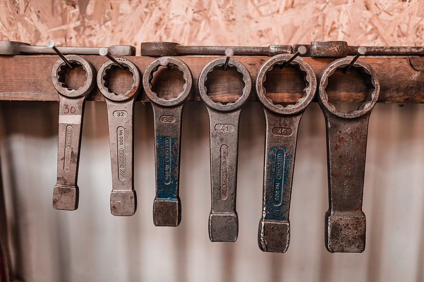 Vintage rusty wrenches hanging on wooden rack in workshop