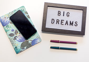 Flat lay of smartphone, journal, and 'Big Dreams' lightbox sign