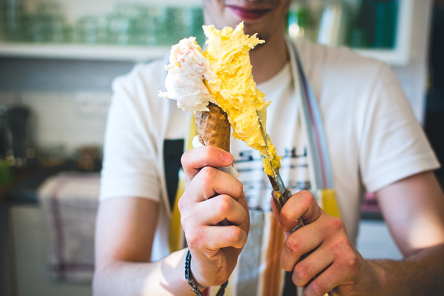Close-up of hands scooping yellow gelato into a waffle cone
