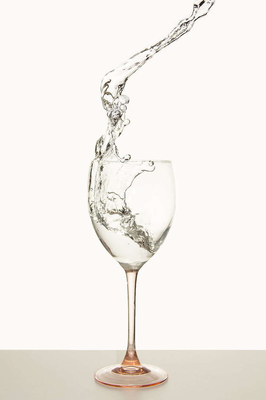 Water Splash Pouring into Clear Wine Glass on White Background