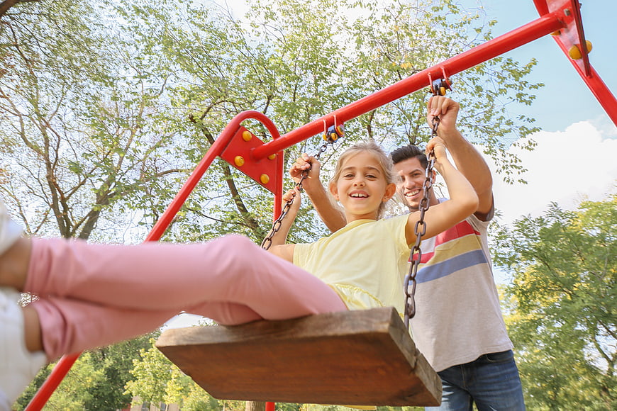 Happy Father Pushing Daughter on Swing in Park