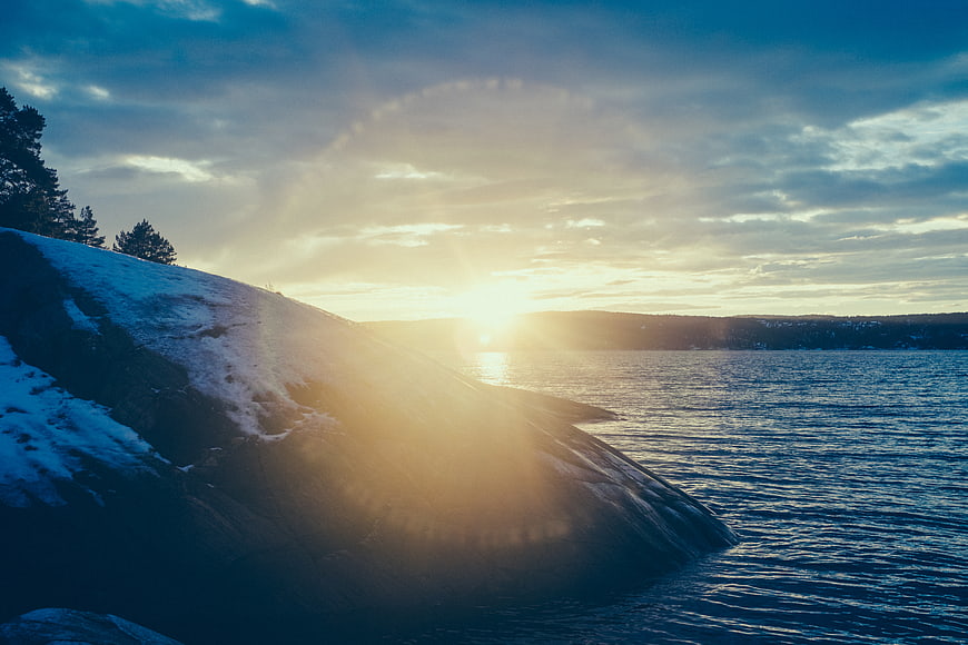 Winter sunset over snowy rocky coastline with sun flare