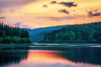 Scenic sunset over a calm lake with forested hills and colorful sky