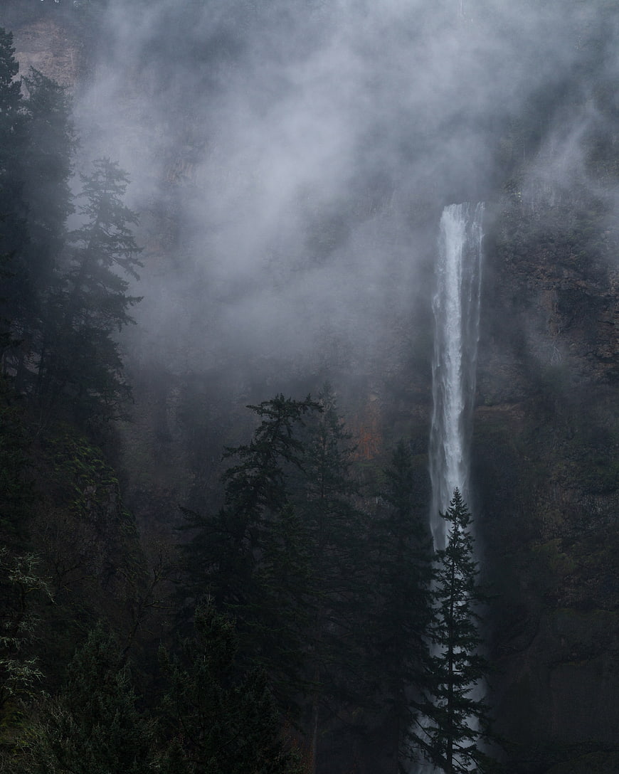 Misty waterfall cascading through dark evergreen forest