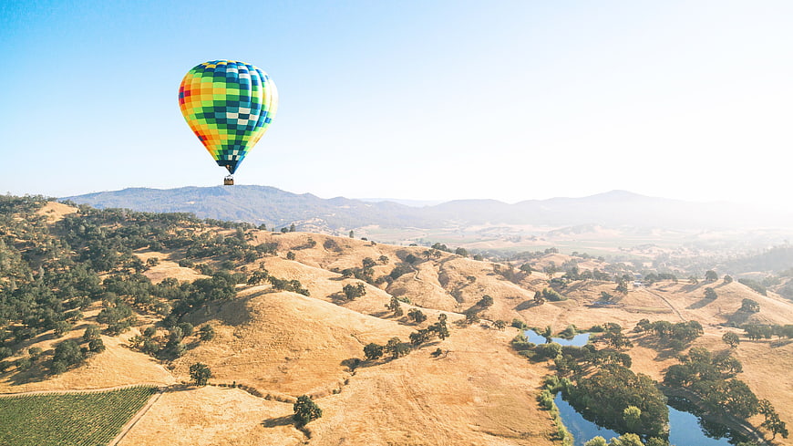 Colorful Hot Air Balloon Flying Over Golden Hills and Lake