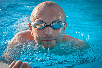 Close-up of bald male swimmer with goggles in blue pool