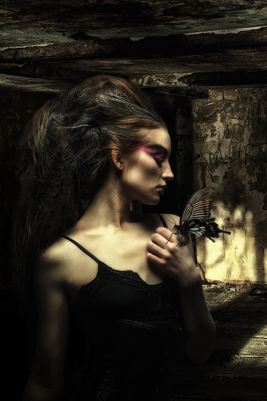 Dark moody portrait of woman with butterfly in ruin