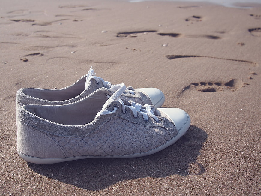 Gray Canvas Sneakers on Sandy Beach with Footprints