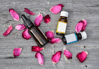 Essential oil bottles with rose petals on rustic wood