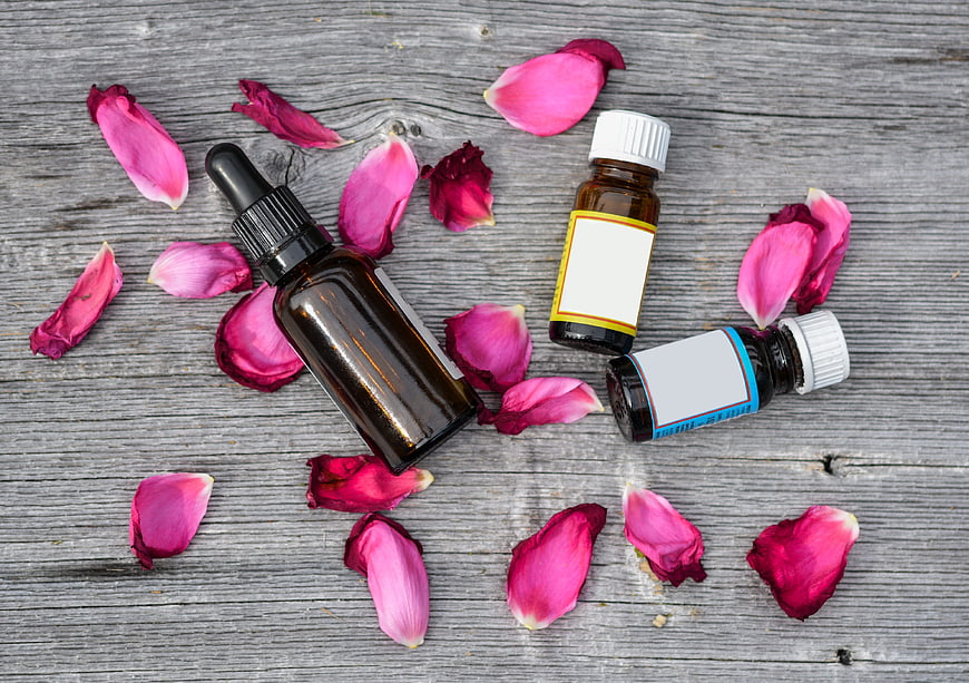 Essential oil bottles with rose petals on rustic wood