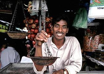Smiling Sri Lankan Shopkeeper Holding Traditional Balance Scale in Market