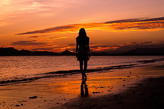 Silhouette of Woman Walking on Beach at Sunset