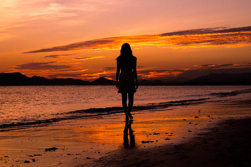 Silhouette of Woman Walking on Beach at Sunset
