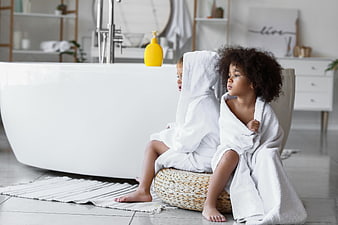 Two children in white bathrobes sitting in a modern bathroom