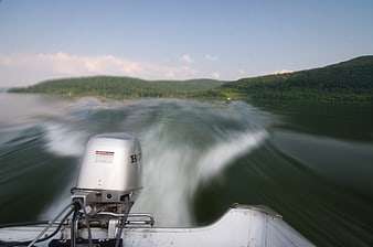 Motorboat wake on lake with forest hills background